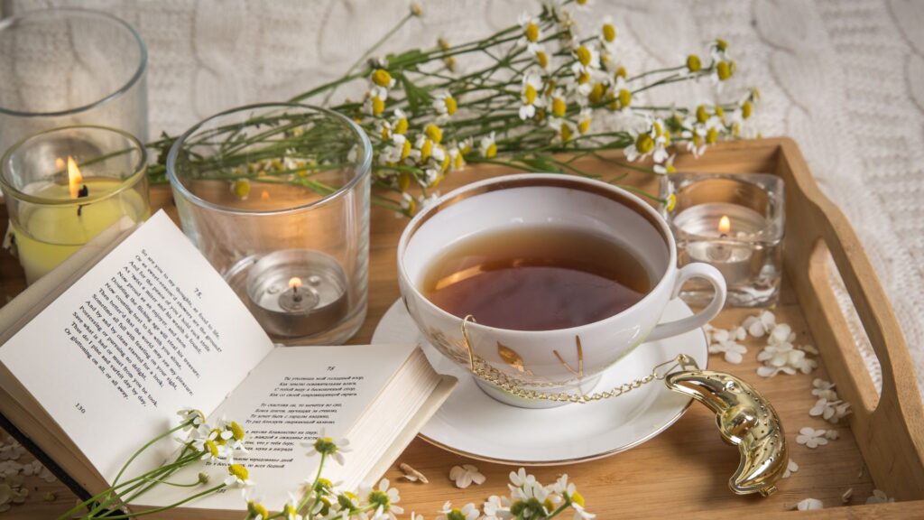 Cup of tea on a tray with flowers, a book and a candle