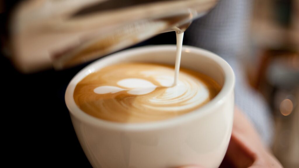 Shot of two hands pouring a coffee latte and latte art
