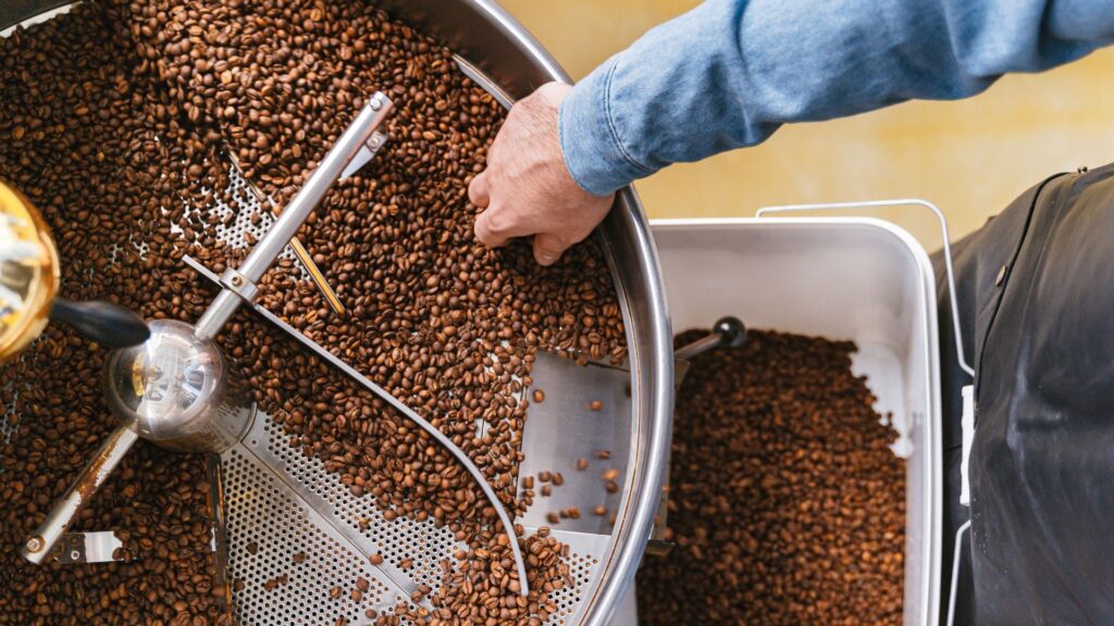 Person holding a bucket to a coffee roasting machine